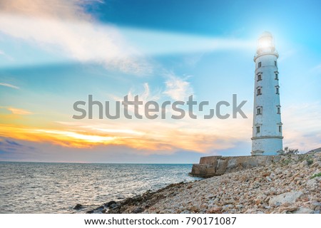 Lighthouse searchlight beam through sea air at night. Seascape at sunset