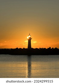 Lighthouse with the sun rising behind it, silhouette lighthouse, calm harbour waters
