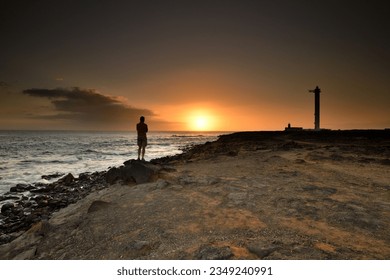 A lighthouse at sunset, A person stands by the sea at sunset, Coastal Landscape with Lighthouse, The Faro de Punta lighthouse in Lanzarote, 