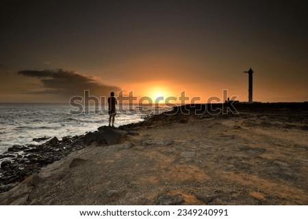 A lighthouse at sunset, A person stands by the sea at sunset, Coastal Landscape with Lighthouse, The Faro de Punta lighthouse in Lanzarote, 