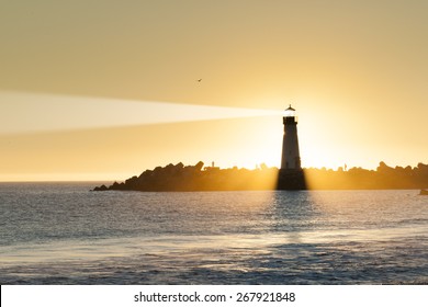 Lighthouse And Surf Boat With Light Beam At Sunset