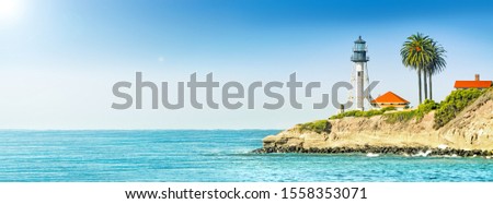 lighthouse tower on cliff in ocean landscape against stormy sea water and blue sky background. Panorama ultra wide side view of marine light beacon with palm tree located on rock. Copy space banner