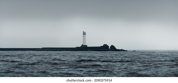 A lighthouse under the dark clouds after the thunderstorm. A view from the sailing boat. Dramatic stormy sky. North sea, Norway. Atmospheric landscape. Symbol of hope and peace