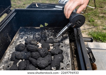 Lighting a home grill with a battery blower, standing in the backyard.
