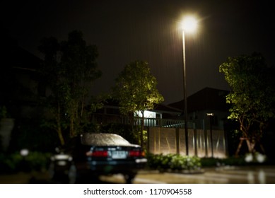 Lighting Lamp Post At The Parking Lot With Blurred Wet Car In The Raining Night