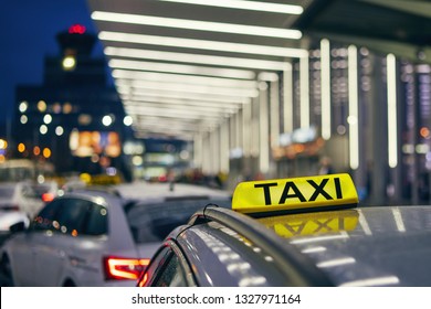 Lighting Taxi Sign On The Roof Of Car Against Airport Terminal At Night. 