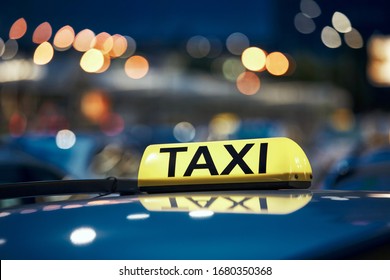 Lighting taxi sign on roof of car on city street at night. 