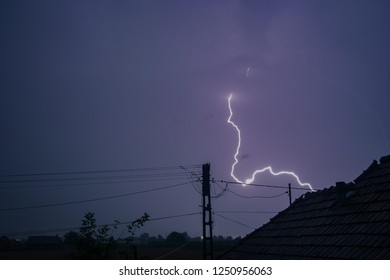 Lightning bolt strikes down to earth in a romanian village with power pole and power lines in the foreground