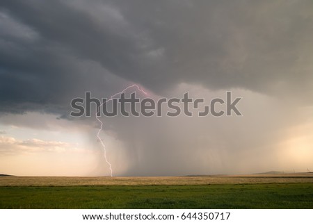 A lightning bolt from a thunderstorm cloud against the backdrop of a countryside landscape.