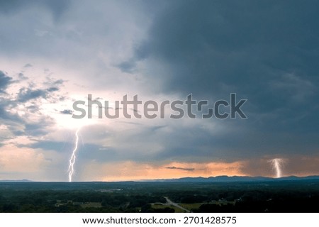 Lightning flashes across dark sky while storm clouds gather over distant mountains during twilight.