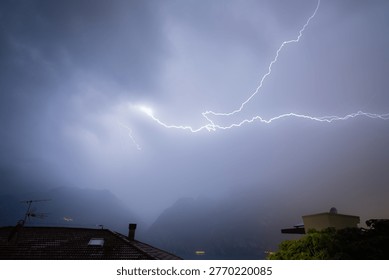 Lightning illuminates a dramatic thunderstorm over lake garda, with mountains and rooftops below