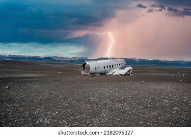 Lightning over broken military airplane wreck at black sand beach. Abandoned airplane in Solheimasandur against stormy sky. Scenic view of tourist attraction on volcanic landscape against cloudscape.