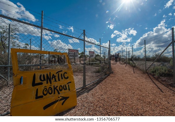 Lightning Ridge, Australia - April 10 2014: People\
looking at the view from Lunatic Lookout, sign posted with a yellow\
car door