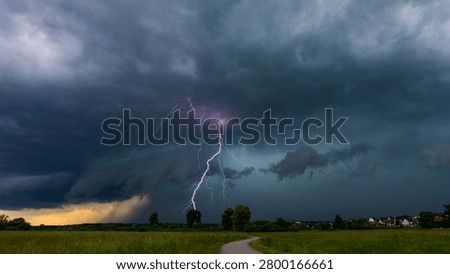Lightning strike illuminating dramatic storm clouds over rural landscape at dusk, Nowy Targ, Poland