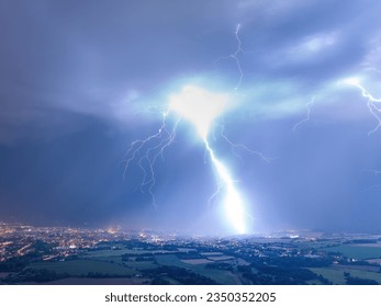 Lightning strike: Panoramic, aerial shot of a city hit by strong lightning. Dramatic, real drone shot of a massive storm. Lightning between the clouds and the ground. 
