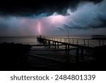 Lightning striking old metal pier, dramatic seaside landscape photo