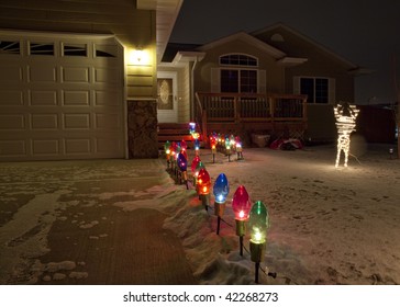 Lights On A Snowy Night Leading The Path Up To A House.