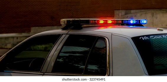 The Lights On Top Of A Police Car At Dusk. The Scene Is Fairly Dark, And The Lights Are Flashing, 