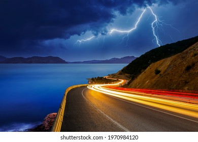 The lights of vehicles on the coastal road at night are getting longer. Lightning falling from the sky to the sea creates a perfect view with the vehicles moving fast on the highway.