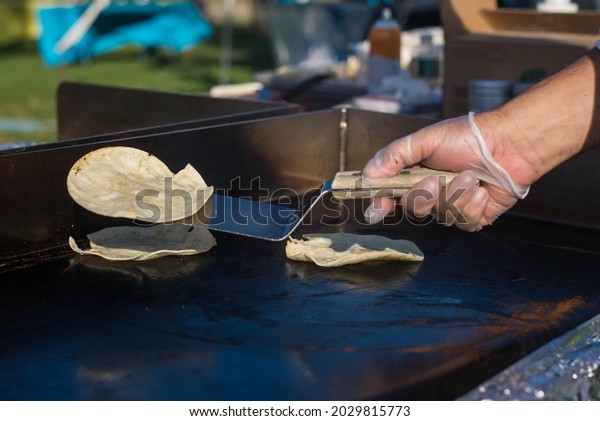 A light-skinned hand in a food prep glove,\
flipping tortillas on a hot\
griddle