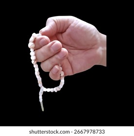 A light-skinned hand holds a string of light-colored patterned prayer beads against a pitch-black background. The prayer beads appear to be made of agate, with tassels at the ends