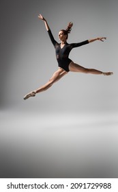 Lightweight Ballerina In Pointe Shoes And Black Bodysuit Jumping On Dark Grey