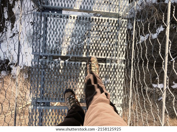 lightweight boots and legs\
of man on the spectacular suspension bridge made of steel ropes and\
metal sleepers