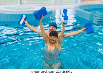 Likable focused caucasian senior adult couple in swimwear exercising with dark blue and white pool buoys while being submerged in swimming pool water. High quality photo - Shutterstock ID 2234268071