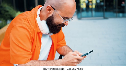 Likable smiling confident young bearded man in glasses using smartphone close up near bussines centre. Social networks outdoor. - Powered by Shutterstock