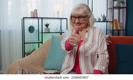 Like. Caucasian senior grandmother looking at camera with toothy smile, raises thumbs up agrees with something or gives positive reply recommends advertisement good. Elderly woman at home room on sofa