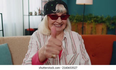 Like. Close-up stylish senior grandmother looking at camera with toothy smile, raises thumbs up agrees with something or gives positive reply recommends advertisement good. Elderly woman at home room