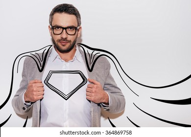 Like a hero. Confident young man adjusting his jacket and looking like superhero in his drawn cape while standing against white background