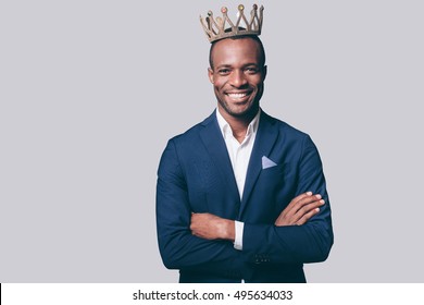 Like A King. Handsome Young African Man In Crown And Smart Casual Jacket Looking At Camera And Smiling Standing Against Grey Background