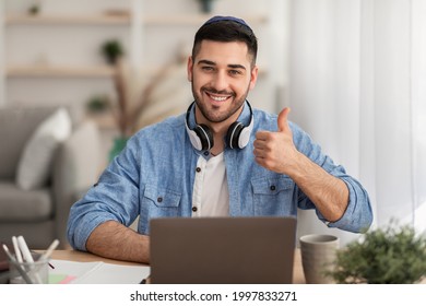 I Like. Portrait Of Happy Jewish Man In Kippa And Headphones Sitting At Desk Using Laptop And Showing Thumbs Up Sign Gesture, Working Or Studying Remotely, Posing To Camera - Powered by Shutterstock