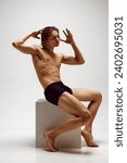 Like a statue. Handsome young man with muscular, athletic, fit body shape posing shirtless in underwear against grey studio background. Concept of men