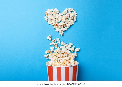 I like watching films. Spilled popcorn in the shape of heart and paper bucket in a red strip on blue background.
