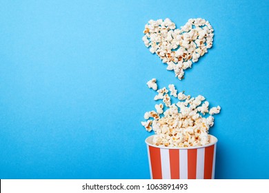 I like watching films. Spilled popcorn in the shape of heart and paper bucket in a red strip on blue background. Copy space for text