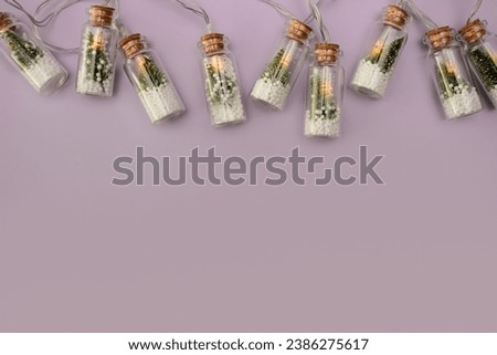 lilac background with unusual creative Christmas lights on the top, in the form of a glass bottle inside the fir tree and snow. copy space, flat lay