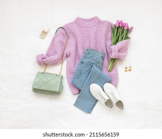 Lilac knitted sweater, blue jeans, white sneakers, green bag, bouquet of tulips flower lie on white background. Overhead view of woman's casual outfit. Trendy stylish women clothes. Flat lay, top view - Shutterstock ID 2115656159