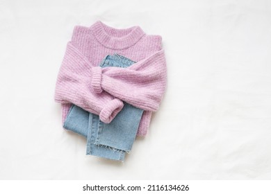 Lilac knitted sweater and blue jeans lie on white background. Overhead view of woman's casual outfit. Trendy stylish women clothes. Flat lay, top view.