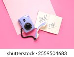 Lilac retro telephone and notebook with text CALL ME on pink background