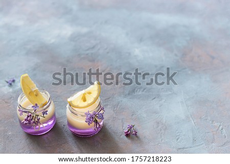 Lilac Vodka Shots drinks with vanilla liqour. Cocktail with Fresh lemon on gray concrete background with lilac flowers. Bar, restaurant menu, recipe. Side view, copy space for text
