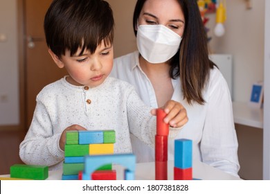 Liltle Preschooler Kid Playing With Wood Blocks And Teacher Educador Help Using Face Mask For Coronavirus Pandemic. Homeshooling. Learning Community. Montessori School
