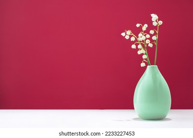 lily of the valley spring flowers in a tiny green vase on table. Vivid magenta background with copy space. Blooming flowers. Greeting card. Border banner