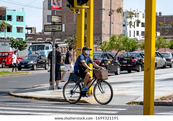 Lima, Peru - April 8 2020: Biker cycling\
in the streets wearing a mask amid coronavirus outbreak in south\
America. Urban area and cars in the\
background.
