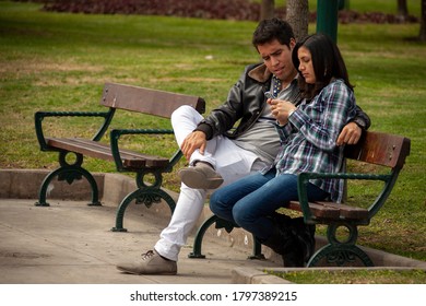 Lima / Peru - August 23, 2013: A Couple Sit On A Park Bench Looking At A Smartphone.