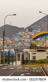 Lima, Peru - December 4, 2008: Colorful Pallet Of Poor Neighborhood Houses Built On Flank Of Tall Mountain Behind Entrance To Parque De La Muralla Under Silver-brown Sky. 