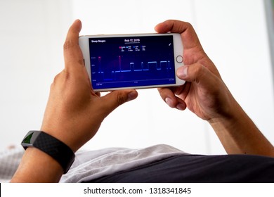Lima, Peru - February 20 2019: Man waking up in the bed and monitoring his sleep night with a sleep-tracking app and a fitbit activity tracker wearable device on his wrist