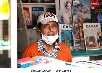 Lima, Peru - March 26 2020: Worker At Kiosk Wearing A Mask Amid Coronavirus Outbreak In South America. Magazines In The Background.