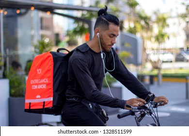 Lima, Peru - March 3 2019: Good Looking Man Riding Bike Working For Rappi Food Delivery Service, Checking The App On His Smartphone. Sharing Collaborative Economy Concept.